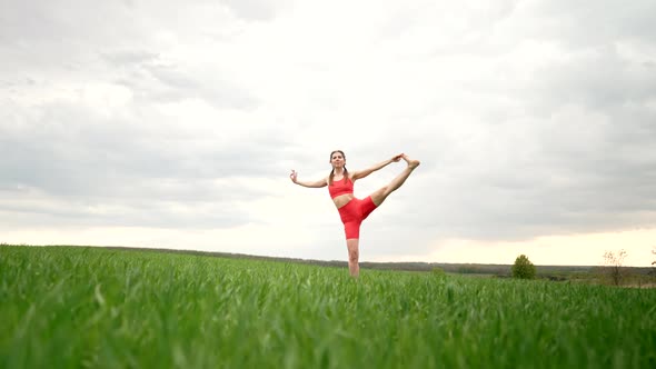Woman in Orange Sports Wear Practicing Yoga  Utthita Hasta Padangushthasana in Green Field alt