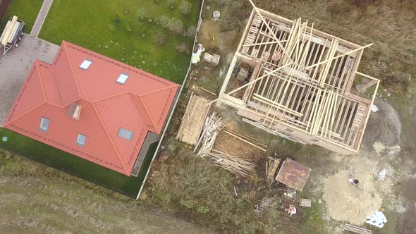 Top down aerial view of two private houses, one under construction with wooden roofing frame  alt