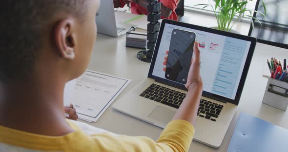 African american businesswoman at desk, reading report, using laptop and smartphone with copy space alt