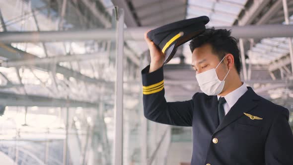 Airliner pilot wearing face mask walking in airport terminal and looking airplane with tired face. alt