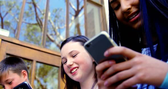 Group of school friends using mobile phone outside school alt