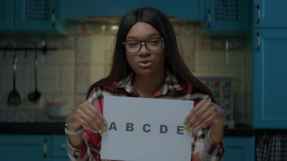Female African American Teacher in Glasses Talking to Camera and Showing Sheet of Paper with ABCDE alt