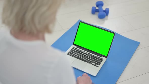 Rear View of Senior Old Woman Doing Yoga While Looking at Laptop with Chroma Key Screen alt