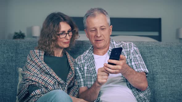 A Middleaged Couple a Man and a Woman are Shopping Online on Their Phone and Smiling Happily While