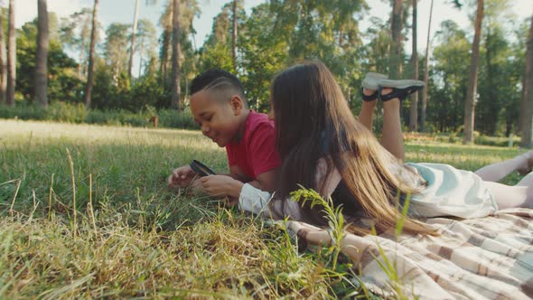School Kids Using Magnifying Glass Looking at Herbs and Bugs Outdoors alt