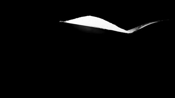 White Sugar Falling From Spoon in Slow Motion Isolated on Black Background