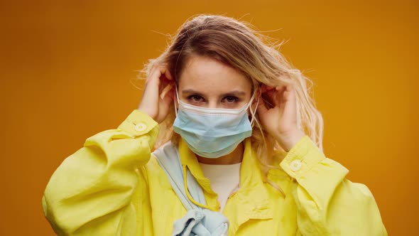 Young Casual Woman Putting on Medical Mask Against Yellow Background alt