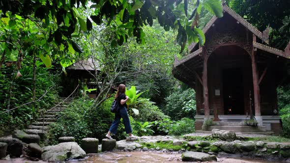 A young woman walking past an ancient temple by waterfall in the forest