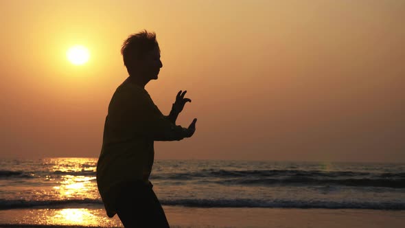 Silhouette of Active Senior Woman Practicing Tai Chi Gymnastic on Sandy Beach. alt