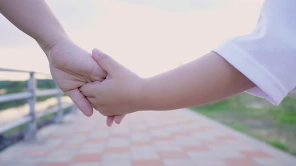 Close up hand of mom and kid holding hand and walking alt