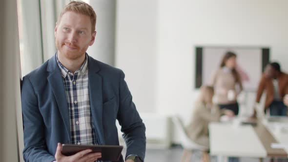 Young handsome businessman standing with digital tablet in front of his team