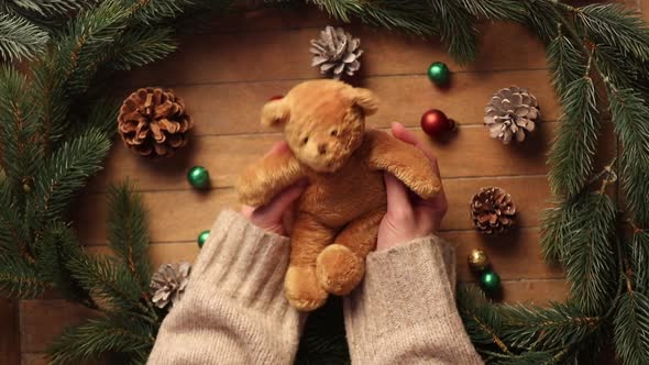 Female hands holding Christmas teddy bear toy on wooden table.