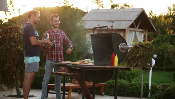Two Male Friends Drinking Beer While Making Barbecue and Showing Ok with Thumbs in Slowmotion alt