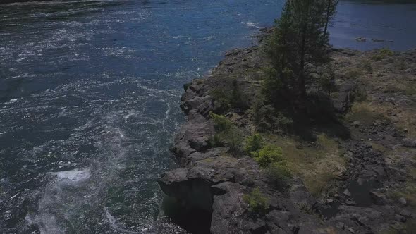 Aerial Drone Traveling Along Flowing Water Shoreline With Small Rocky Islands Below 1
