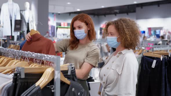 Girlfriends in Medical Masks and Gloves Choose Clothes in Store alt