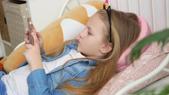 a Pretty Little Girl in a Rim with Cat Ears with a Phone in Bed alt
