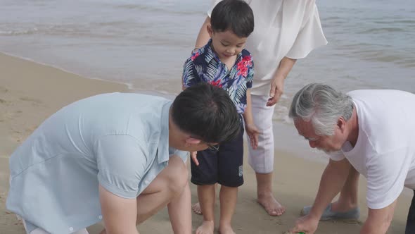 Asian father building sand castle with grandfather for little boy