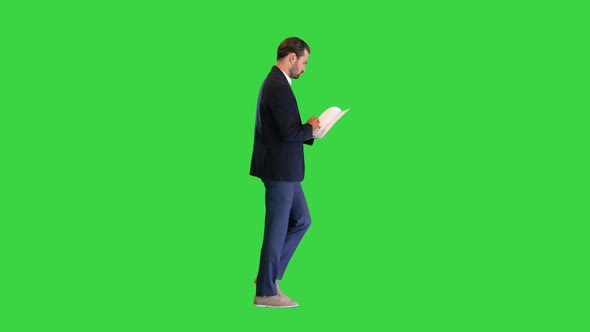 Serious Young Businessman Reading Documents While Walking on a Green Screen Chroma Key alt