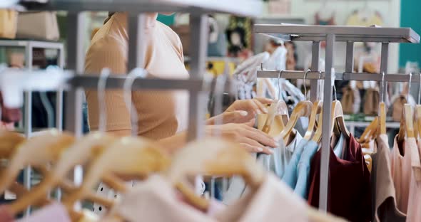 Young Woman Walk Between Rows of Clothes and Looking a Dress in Shopping Mall