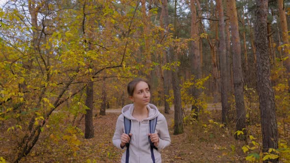 Front View of Young Woman with Backpack Walking in Autumn Park  Steadicam Shot