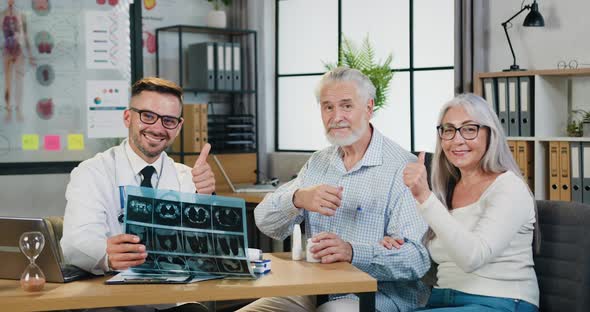 Doctor with Results of X-ray Scan which Looking Into Camera Together with Positive Senior Couple alt