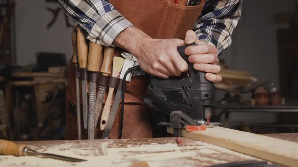 Carpenter is Sawing a Wood Plank with Electric Jig Saw Machine in Carpentry Workshop alt