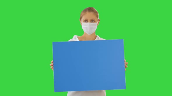 Beautiful Businesswoman in Protection Mask Holding Blank Board on a Green Screen, Chroma Key. alt