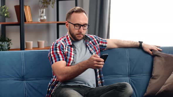 Confident Business Man Sitting on Couch at Home Surfing Mass Media Mobile Application Bad News alt