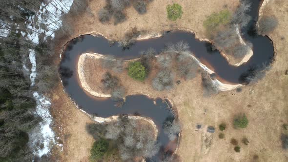 AERIAL: River Flows Near Forest with Part of it Covered in Snow