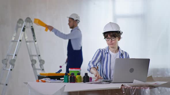 Woman in Safety Helmet Smiles and Enjoys Choosing Paint Color on a Color Palette for New Walls at a alt