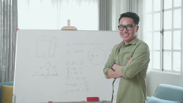 Asian Male Teacher With Glasses Crossing Arms And Smiling To Camera While Teaching Math At Home alt
