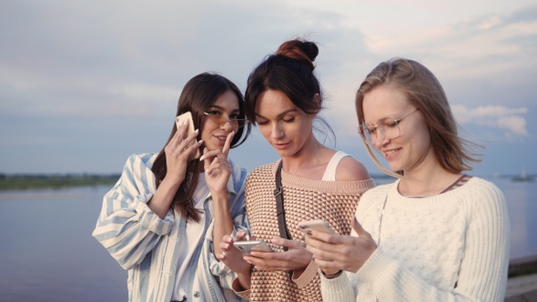 Trendy friends walking together using their smartphones. alt