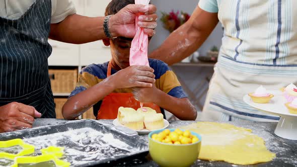 Grandfather and father assisting boy to make cupcakes alt