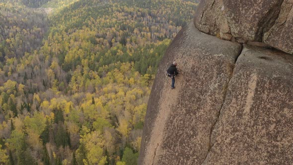 A Man Climbs a Rock with a Wonderful View of the Autumn Forest