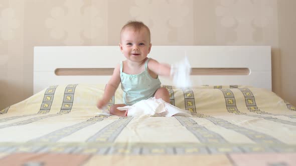 Baby Is Playing with White Napkins While Sitting on the Bed. Emotional Kid. The First Joy Is Simple