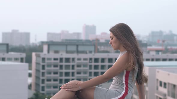 Lady in Knitwear Dress Sits on Roof Against Beautiful View alt