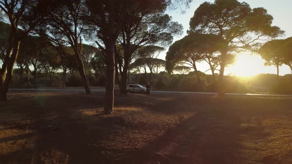 Aerial view of a man flying drone through the trees at sunset in Greece. alt