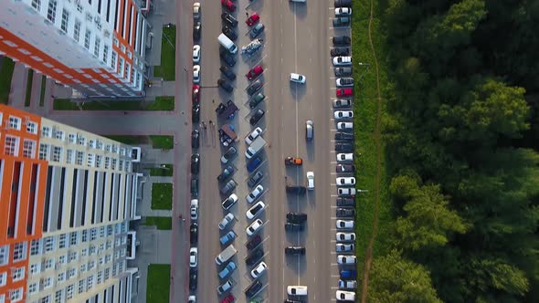 A Drone Flies Over a Road with Moving Cars. Forest and High-Rise Buildings