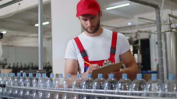 Young Factory Man in Uniform Making Notes on Clipboard at Water Production Factory