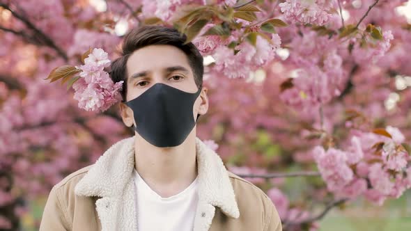 Pandemic, portrait of a young man on a woolen jacket on black virus protective mask on street.  alt