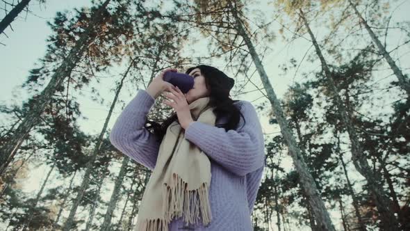 Pretty Lady in Sweater Holds Cup of Drink in Winter Forest