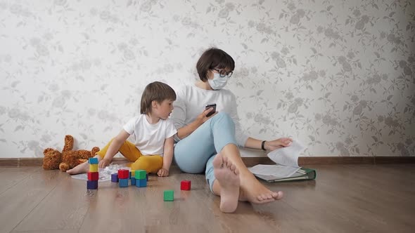 Mom and Son Sit at Home Quarantine Because of Coronavirus COVID19. Mother Sits with Smartphone, Son alt