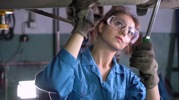 Car Mechanic Girl Mechanic in the Workshop Stands Near the Car Lifted Up on the Elevator alt