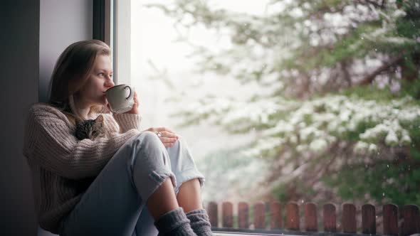 A Beautiful Young Girl Sits on the Windowsill with a Cute Cat