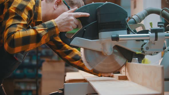 Carpentry - a Man Woodworker Cutting the Wooden Detail with a Sharp Circular Saw alt