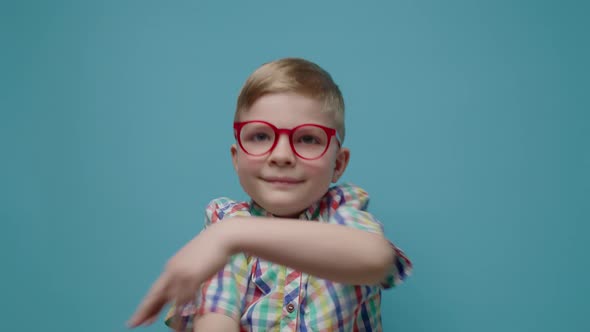 Charming Boy Wearing Eyeglasses Dancing Looking at Camera on Blue Background alt