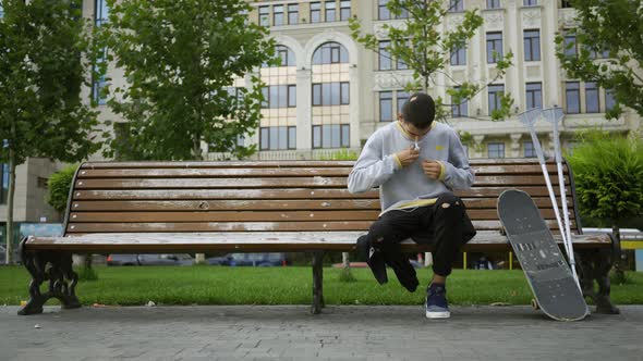 Attractive Young Man Sitting on the Bench in the Park Listening To Music on His Cellphone Then alt
