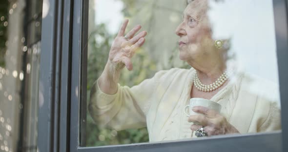 Senior Grandma Woman Drinking Cup of Tea or Coffee Near Window Looking Outside Worried or Sad or