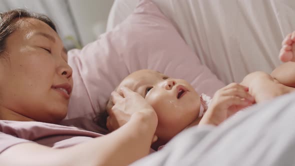 Loving Asian Mom Bonding with Baby Daughter on Sofa alt
