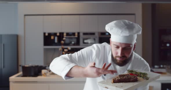 Young Handsome Chef in White Uniform Holding Wooden Board with Ready Beef Steak alt